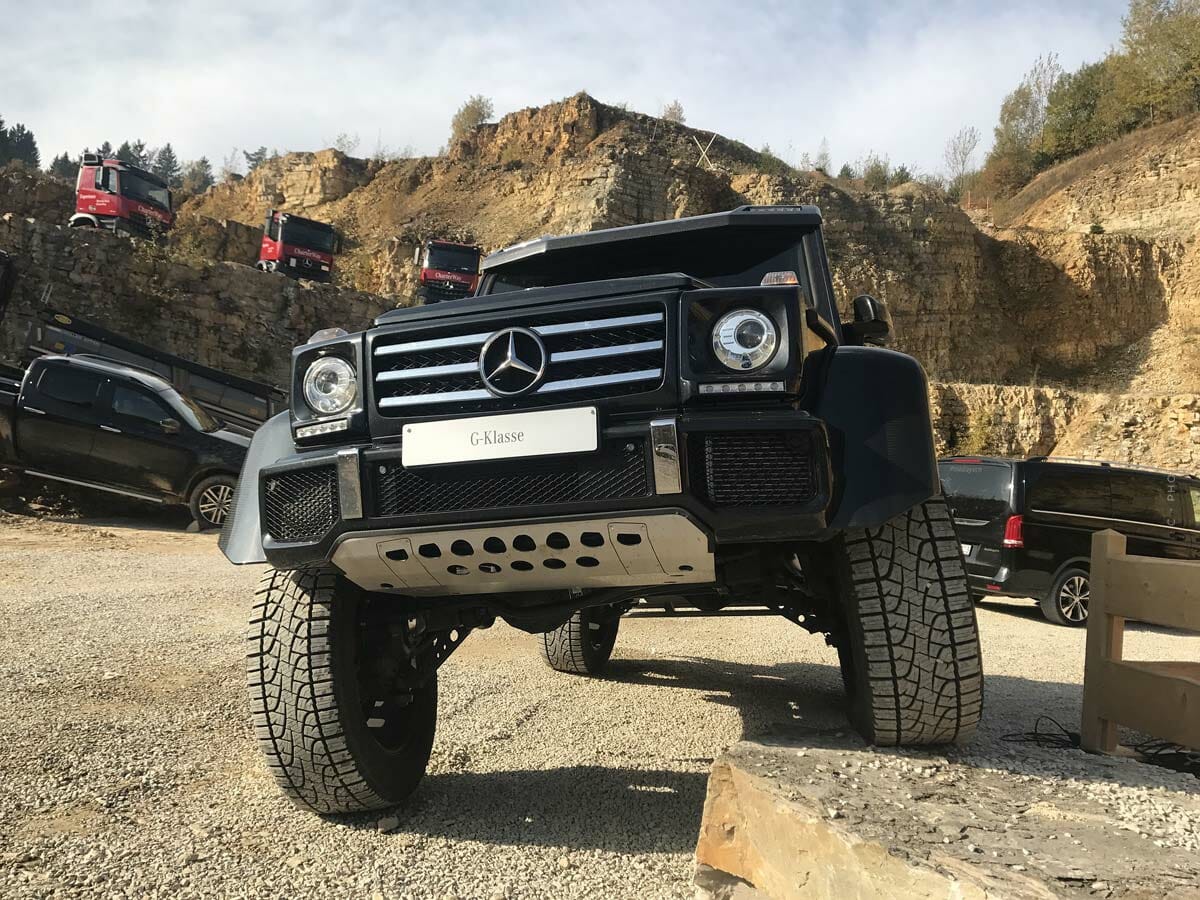 Une voiture tout-terrain noire se tient avec un pneu sur une pierre dans un environnement sablonneux.