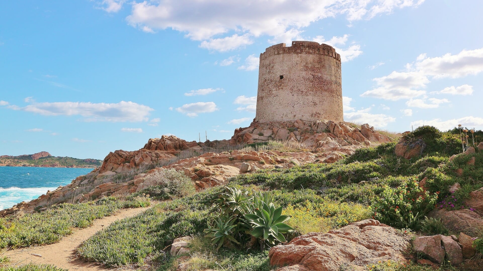 Les ruines d'une tour se dressent sur une colline et la mer est visible en arrière-plan