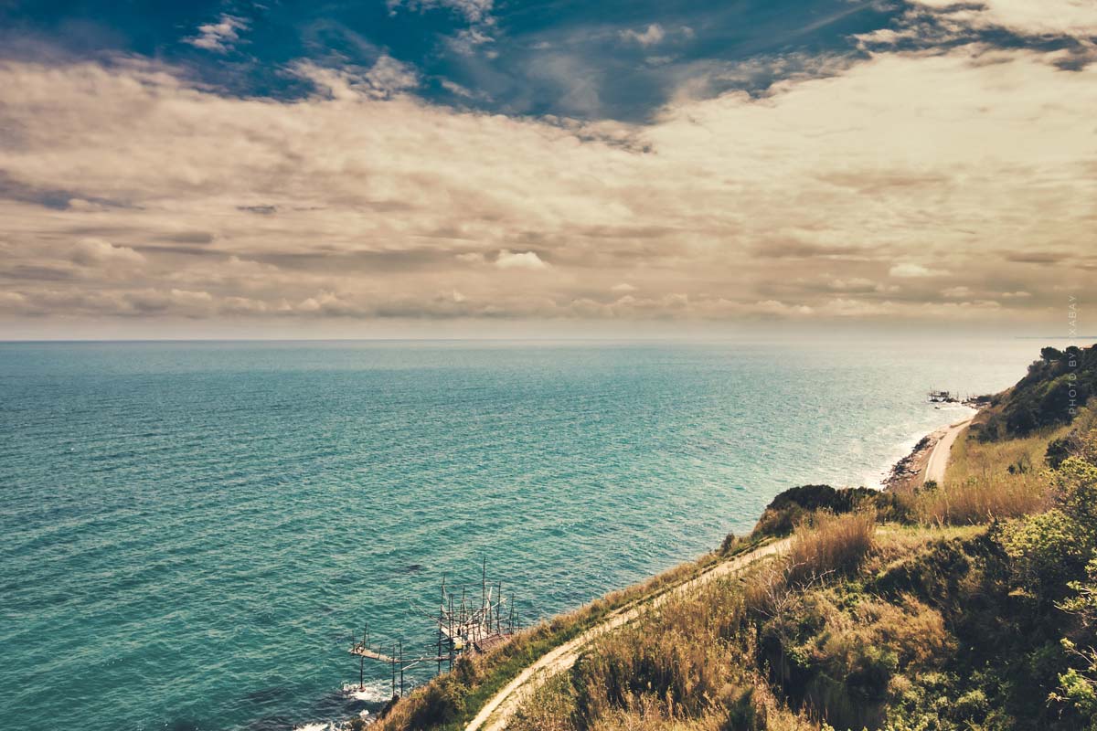 Une route longe un versant de colline verdoyant au bord de la mer bleue.