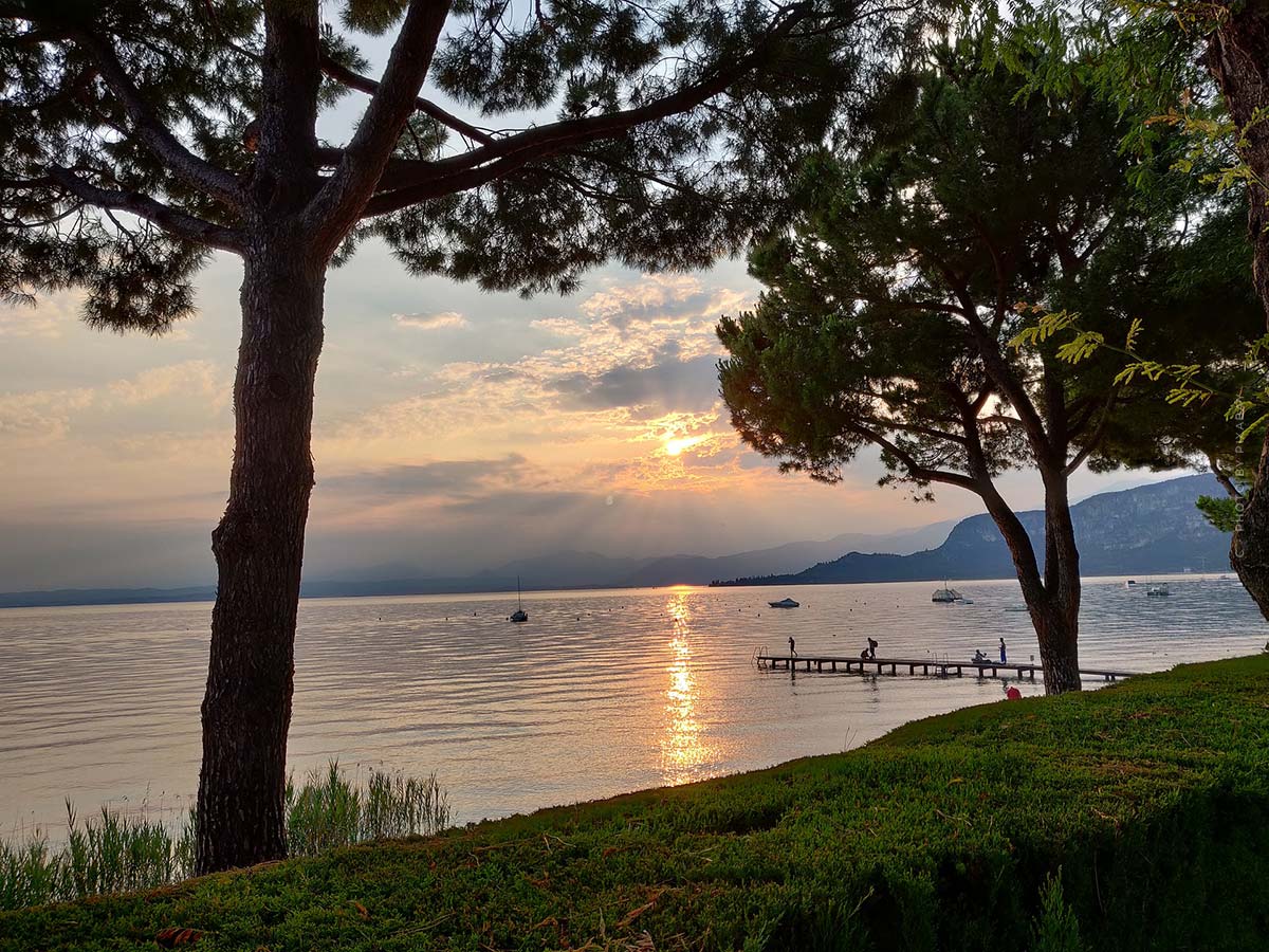 Le coucher de soleil sur le lac est encadré par deux arbres.