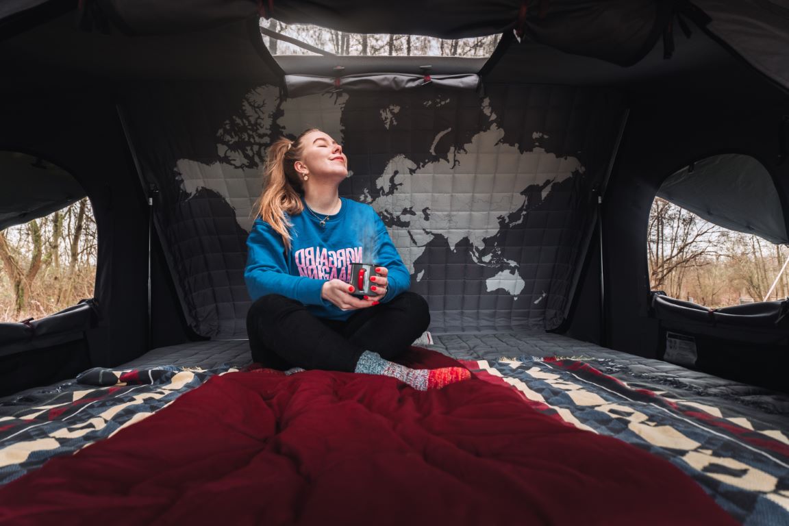 Une femme se détend avec une tasse de thé dans sa tente de toit Toyota Hilux