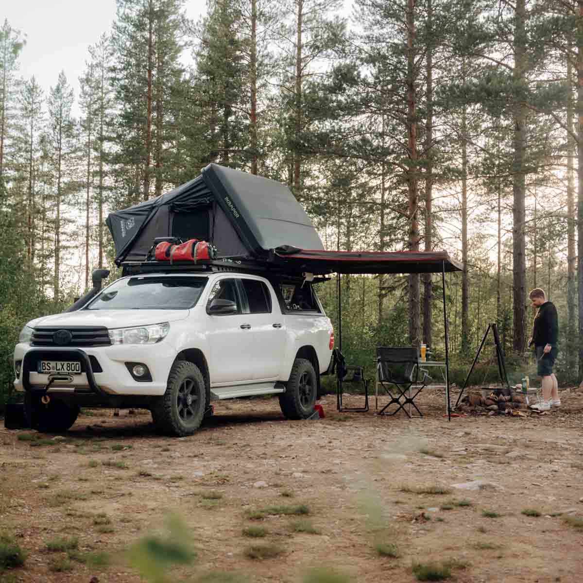 Un homme campe dans la forêt avec son pick-up équipé d'une tente de toit et d'un auvent