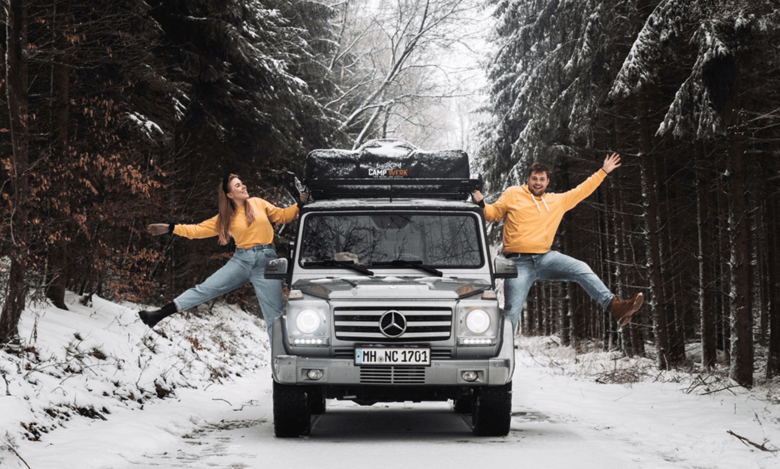  Couple en tenues assorties à côté de leur voiture avec une tente de toit Campwerk sur une route enneigée dans la forêt