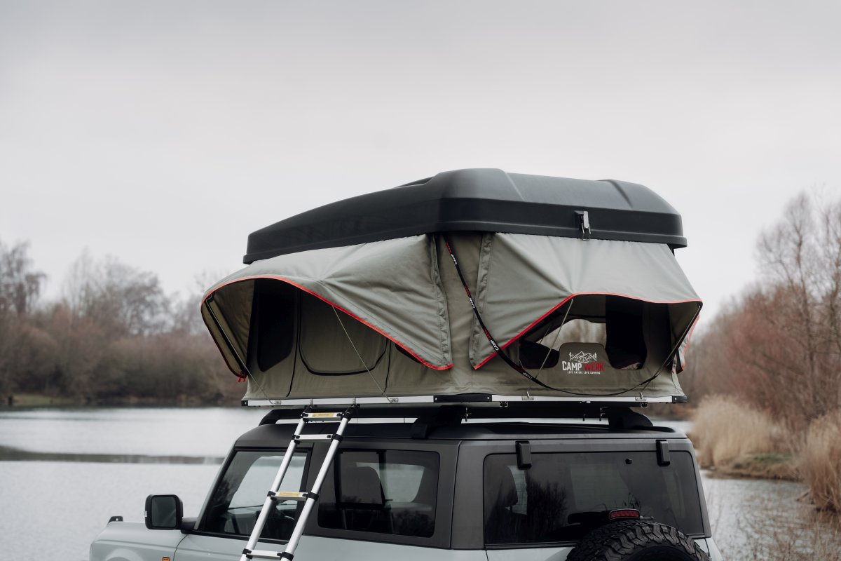 Gros plan d'une tente de toit CAMPWERK sur une voiture grise garée au bord d'un lac