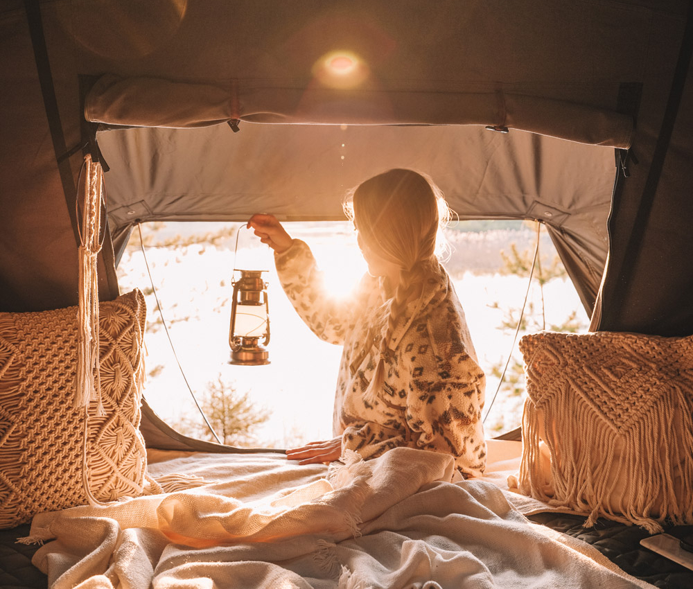 Jeune femme assise avec une lampe de camping dans la tente de toit au coucher du soleil