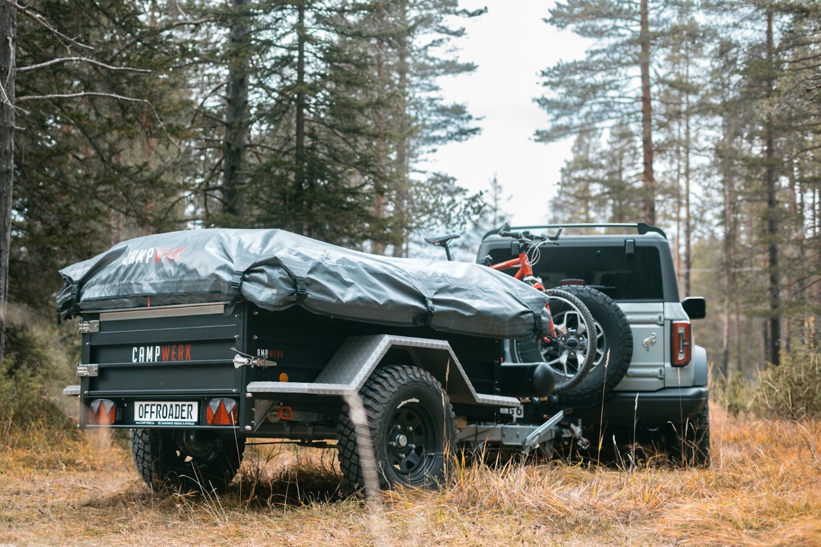 Une voiture avec une remorque de tente dételée sur un chemin forestier