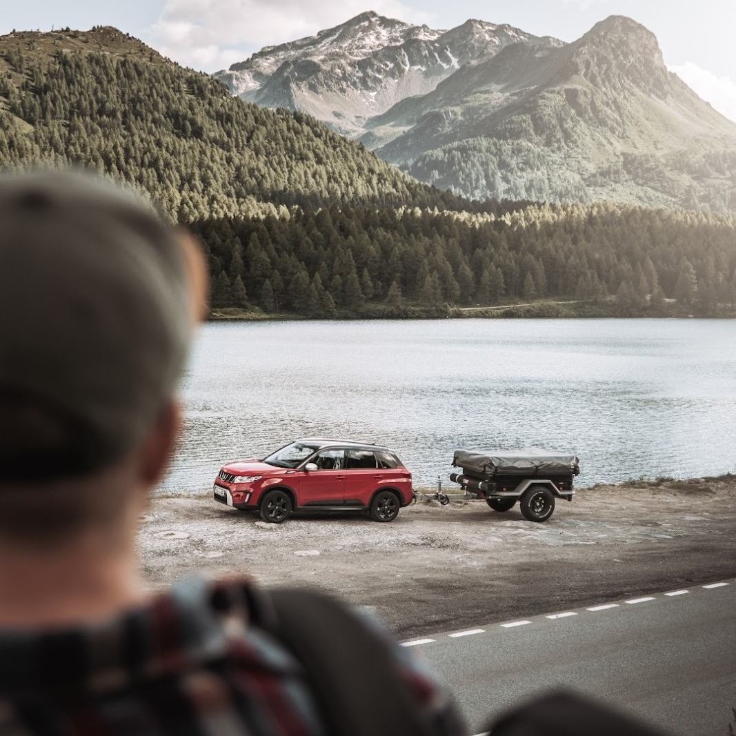 Une personne regarde une voiture avec une remorque de tente dételée au bord du lac